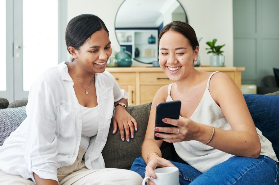 happy-woman-friends-laughing-with-phone-sofa-social-media-communication-funny-joke-home-female-person-with-smile-mobile-smartphone-friendly-chat-online-browsing-house
